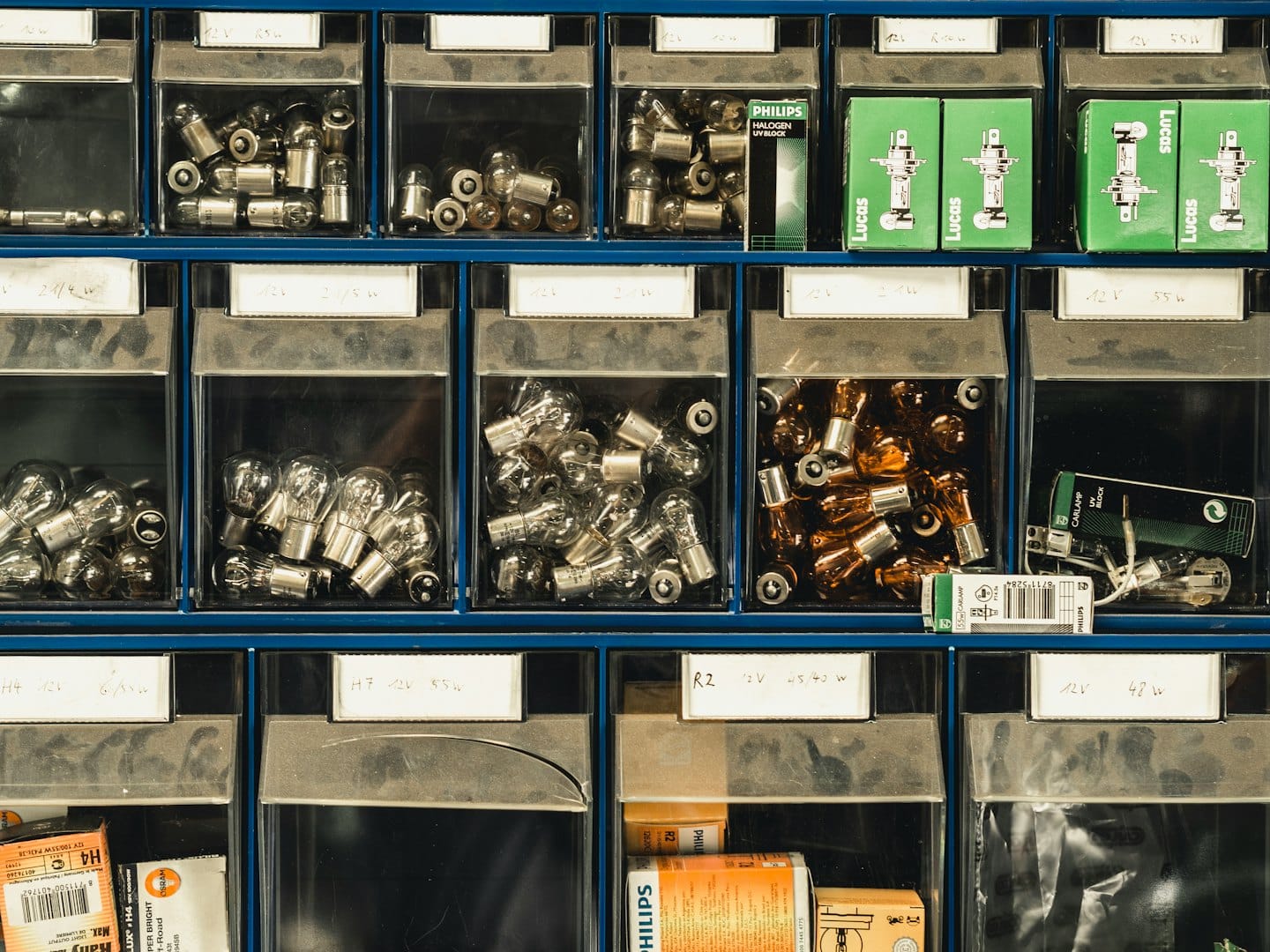 Niebieski metalowy organizer wypełniony oznaczonymi żarówkami samochodowymi.